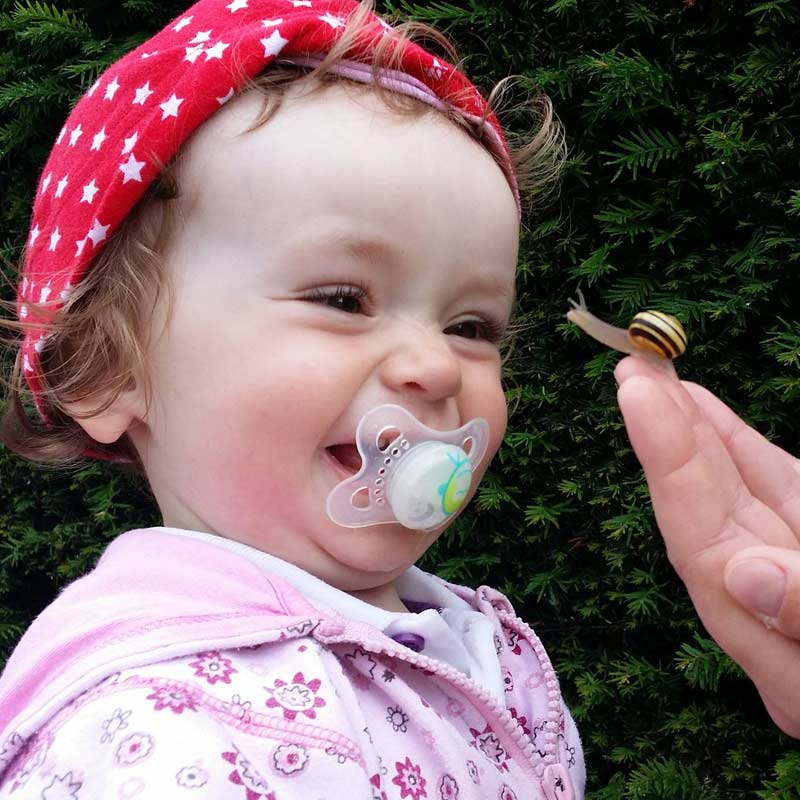 Kind mit Nuckel freut sich über eine kleine Schnecke